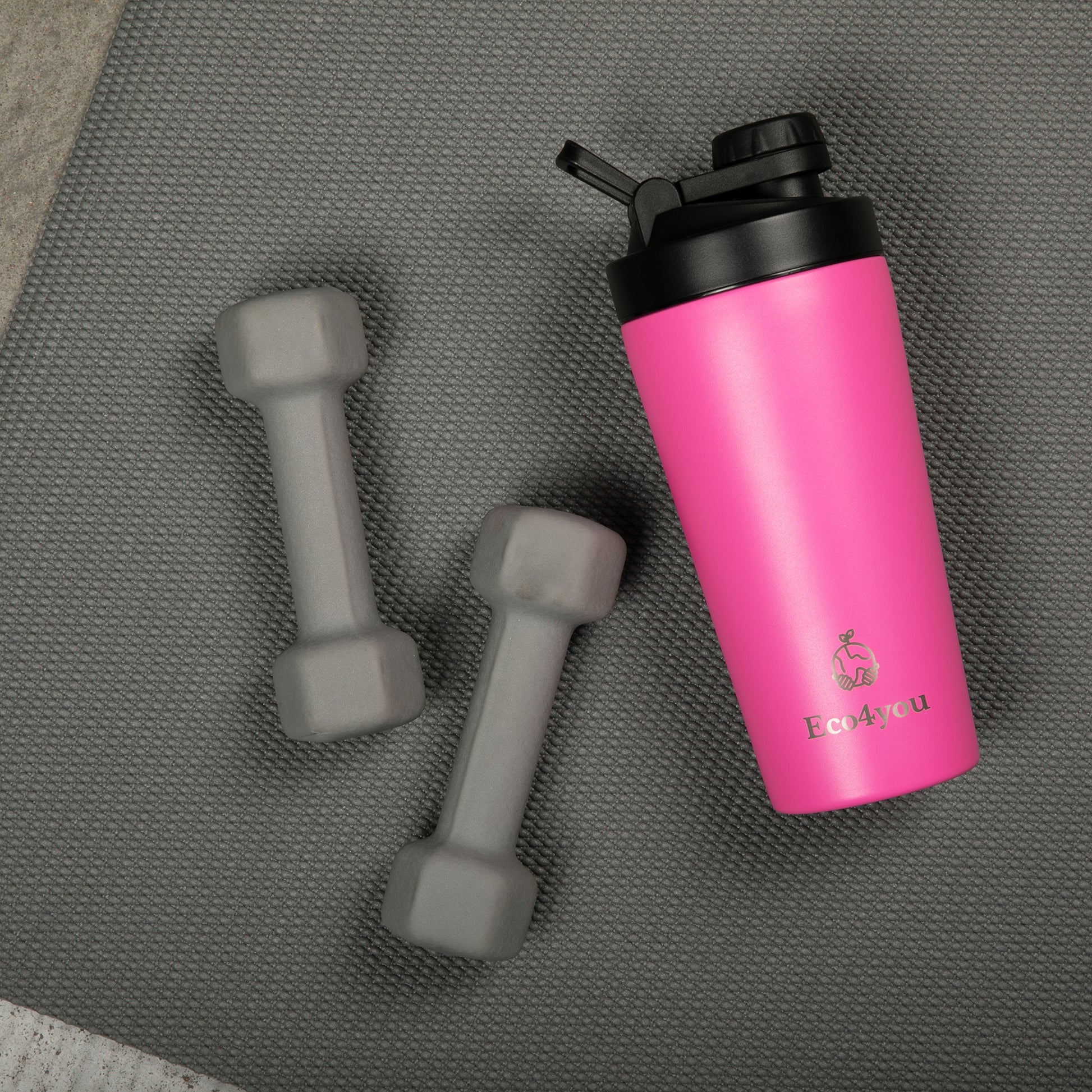 Eco4you pink stainless steel shaker bottle next to two gray dumbbells on a workout mat.